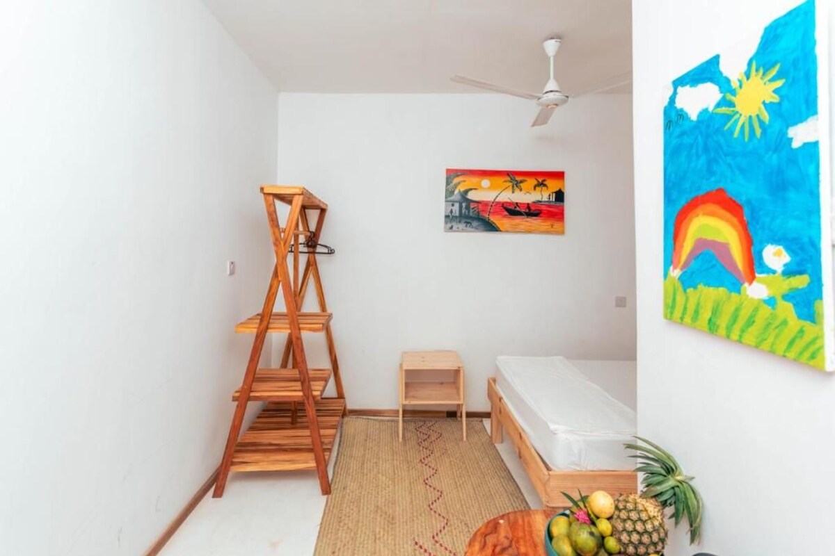 A room with a wooden ladder, a small wooden table, a bed, and a painting on the wall.