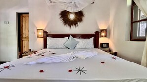 A neatly made bed with a white bedspread, pillows, and decorative items like a star and rose petals. - Tiki Beach Club & Resort (Paje)