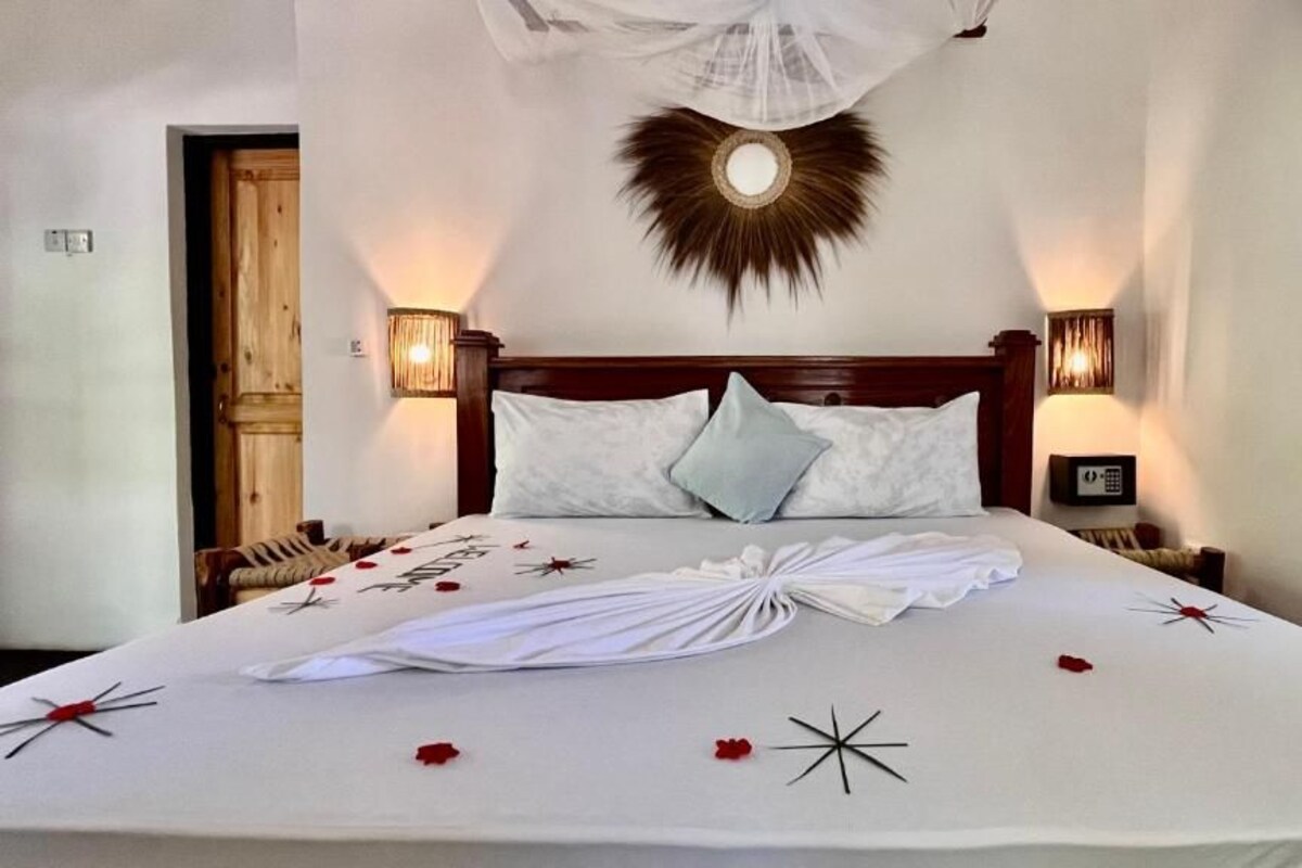 A neatly made bed with a white bedspread, pillows, and decorative items like a star and rose petals.
