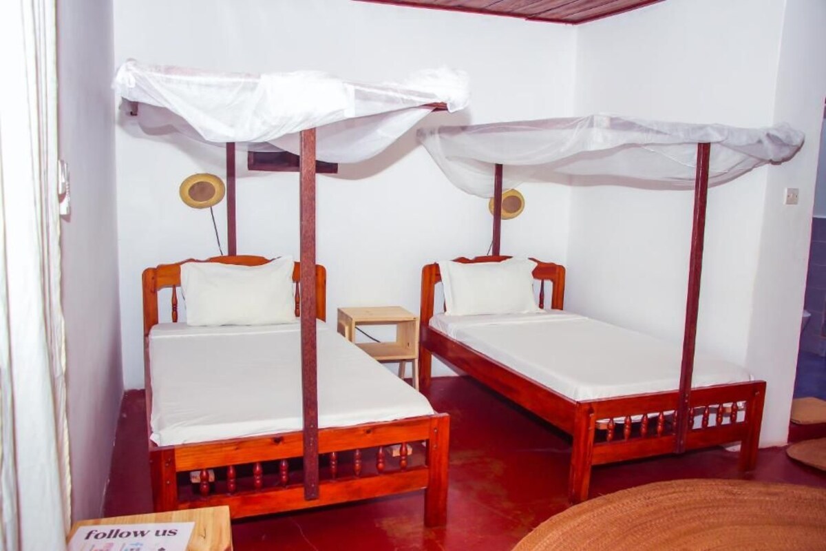A room with two wooden beds, each with a canopy. There is a small wooden stool and a woven basket on the floor.