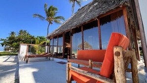 A beachside hut with a thatched roof, wooden furniture, and large windows overlooking the ocean. - Tiki Beach Club & Resort (Paje)
