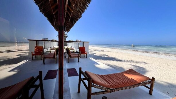 A beachside lounge with a thatched roof, wooden furniture, and a view of the ocean. - Tiki Beach Club & Resort (Paje)