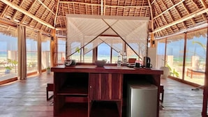 A beachside room with a wooden floor, a small bar area, and a view of the ocean. - Tiki Beach Club & Resort (Paje)