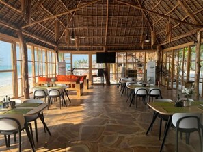 A spacious indoor area with a thatched roof, large windows, and a view of the beach.