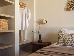 Une chambre à coucher avec un lit, une table de chevet ornée d’un vase, une lampe suspendue et une armoire avec des étagères.