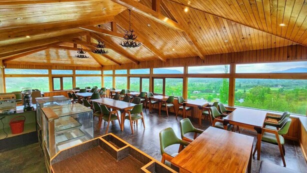 A spacious dining area with high ceilings and large windows offering a view of the countryside. - The Walnut Creek Hotel (Anantnag)