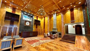 A spacious lobby with a herringbone wooden floor, a fireplace, a chandelier, and a stone accent wall. - The Walnut Creek Hotel (Anantnag)