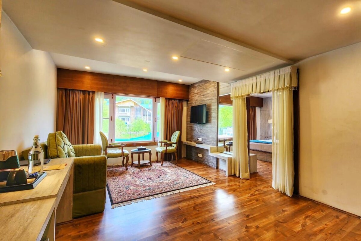 A spacious living area with a wooden floor, a sofa, a coffee table, and a TV mounted on the wall.