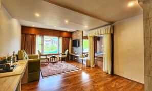 A spacious living area with a wooden floor, a sofa, a coffee table, and a TV mounted on the wall. - The Walnut Creek Hotel (Anantnag)