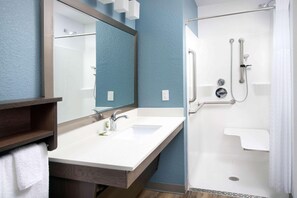 A bathroom with a double sink, a mirror, a shower with a grab bar, and a towel rack. - Woodspring Suites Orlando International Drive (Orlando)