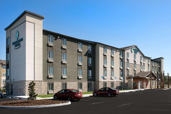 Un hôtel à plusieurs étages, doté d’une façade en pierre, de nombreuses fenêtres et d’un parking rempli de voitures.