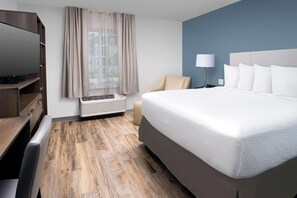 A hotel room with a large bed, a TV, a desk, and a window with curtains. - Woodspring Suites Orlando International Drive (Orlando)