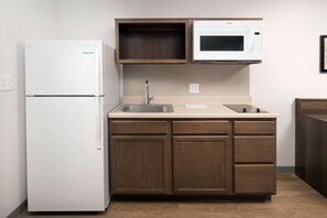 A compact kitchen with a white refrigerator, a microwave, a sink, and wooden cabinets. - Woodspring Suites Orlando International Drive (Orlando)