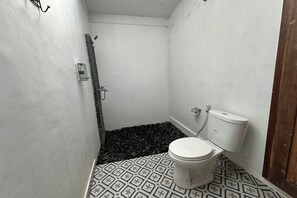 A small, compact bathroom with a toilet, a shower, and a patterned floor. - Mahayana Guest House Ubud By Zuzu (Ubud)