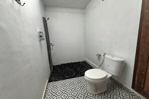 A small, compact bathroom with a toilet, shower, and a patterned floor. - Mahayana Guest House Ubud By Zuzu (Ubud)