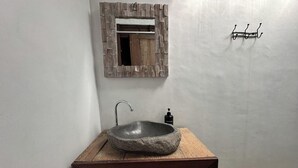 Un baño con un lavamanos de piedra, un mueble de tocador de madera, un espejo con marco rústico y un dispensador de jabón para manos.