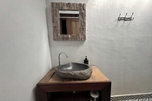 Un baño con un lavamanos de piedra, un mueble de tocador de madera, un espejo con marco rústico y un dispensador de jabón para manos.