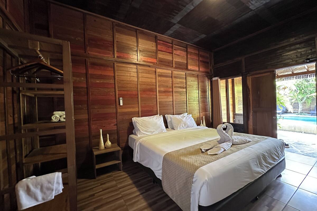 A wooden-paneled room with a bed, a wooden shelf, and a small table.