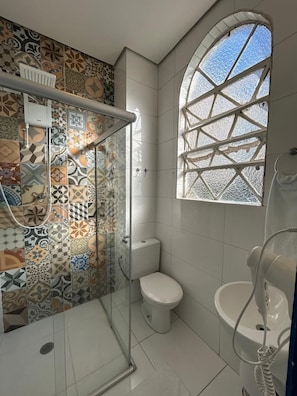 Een badkamer met douche, toilet en wastafel, met tegeldecoratie en een groot raam.