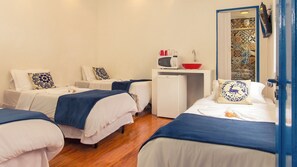 Een hotelkamer met drie bedden, een kleine kitchenette en een badkamer met een betegelde douche.