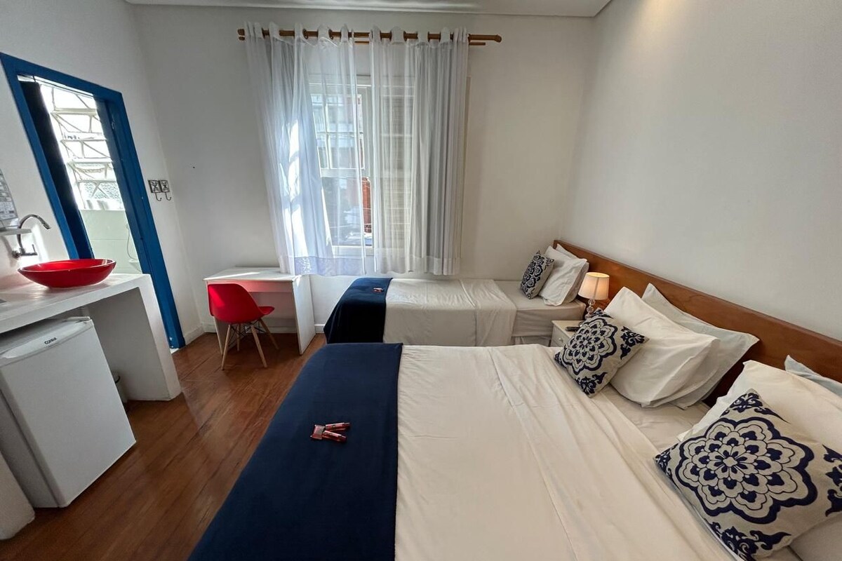 Een hotelkamer met een bed, een bureau, een rode stoel, een kleine koelkast en een raam met gordijnen.