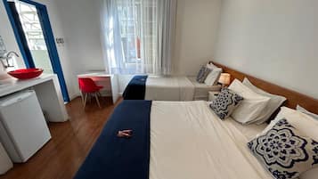 Quarto de hotel com uma cama, uma escrivaninha, uma cadeira vermelha, um frigorífico pequeno e uma janela com cortinas.
