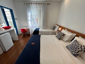 Een hotelkamer met een bed, een bureau, een rode stoel, een kleine koelkast en een raam met gordijnen.