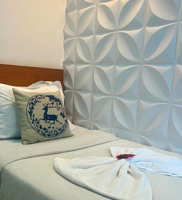 Uma cama com cabeceira estampada, um travesseiro com desenho de veado e uma toalha sobre a cama.