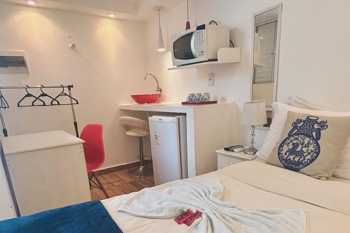 Een hotelkamer met een bed, een bureau, een stoel, een magnetron en een kleine koelkast.