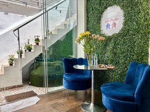 Een modern interieur met een trap, een blauwe stoel, een tafel met een bloevas en een groene muur met een logo.