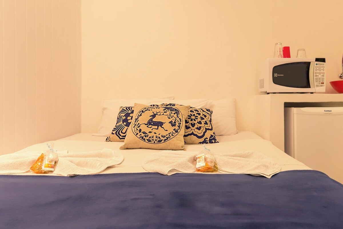 Een hotelkamer met een bed, kussens, een magnetron, een spoelbak en een kleine koelkast.