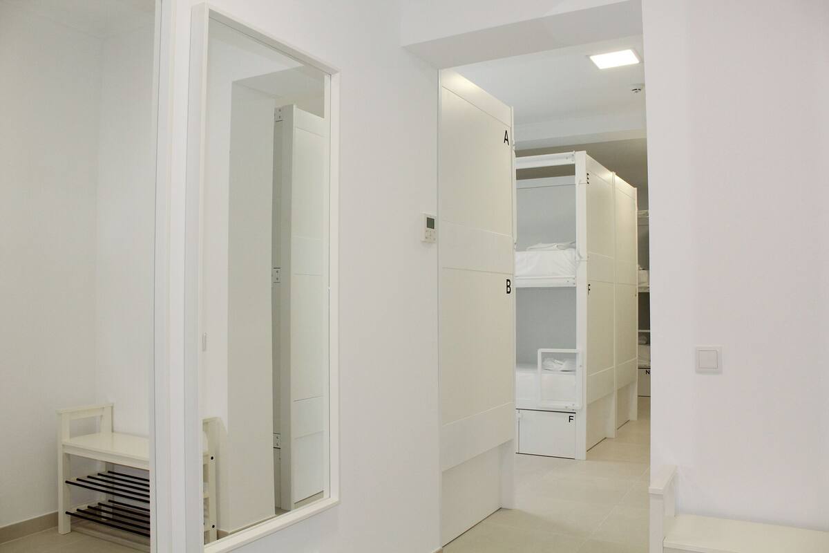 A corridor with white walls, a mirrored closet door, and a bench.