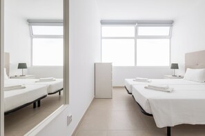 A hotel room with two beds, a large window, a bedside table with a lamp, and a wardrobe. - Dunas Hostel & Guesthouse (Portimão)