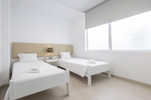 A modern hotel room with two single beds, a nightstand with a lamp, and a large window providing natural light. - Dunas Hostel & Guesthouse (Portimão)