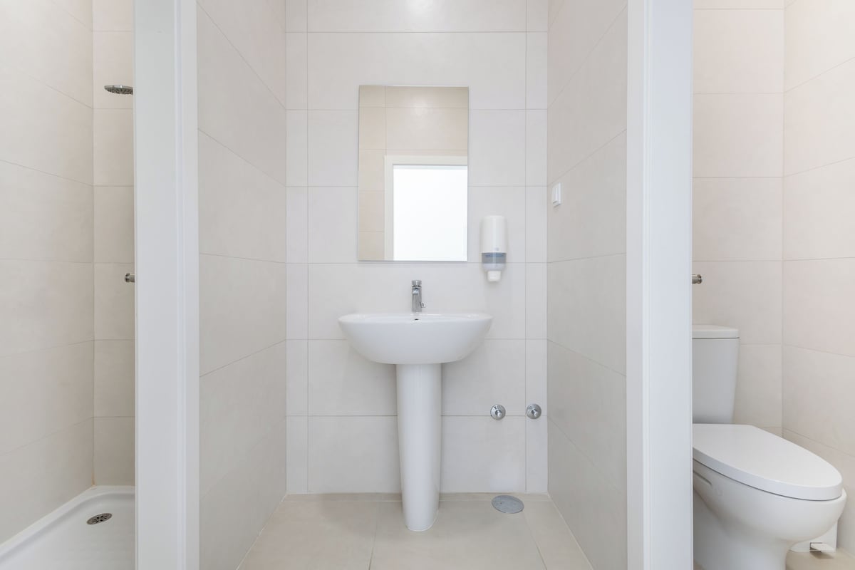 A bathroom with a pedestal sink, a mirror, and a toilet.
