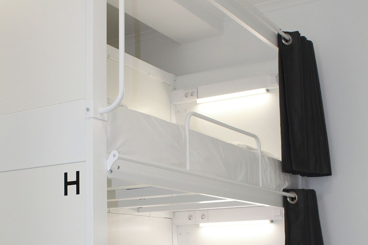 A bunk bed with a pull-up ladder, a small enclosed storage space, and a curtain on the right side.