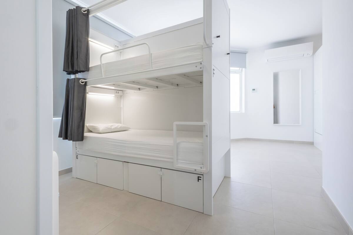 A bunk bed with storage drawers, a window with curtains, and a white door.