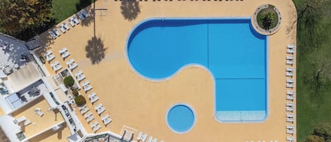 Vista aérea de un hotel con una piscina grande, varias zonas de descanso y un jardín ajardinado.