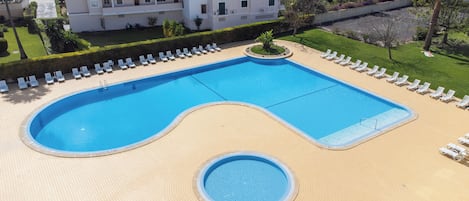 A rectangular swimming pool with a small circular section in the middle, surrounded by lounge chairs and a paved deck.