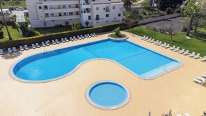 A rectangular swimming pool with a small circular section in the middle, surrounded by lounge chairs and a paved deck. - Dunas Hostel & Guesthouse (Portimão)