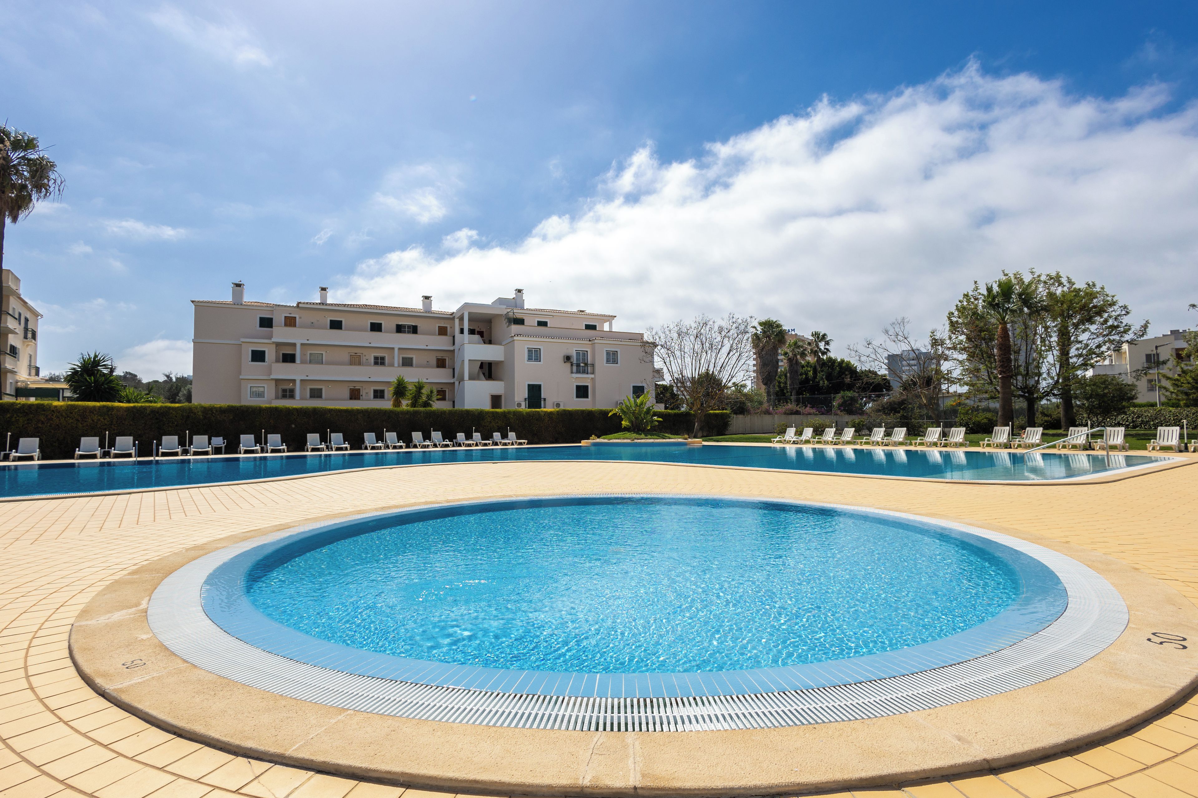 Una piscina con sillas de descanso y un edificio al fondo.