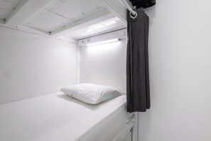 A single bed with a white pillow and a black curtain in a small, white room with a ceiling light. - Dunas Hostel & Guesthouse (Portimão)