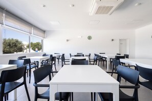 A modern classroom with white tables and black chairs, large windows, and a ceiling with recessed lighting. - Dunas Hostel & Guesthouse (Portimão)