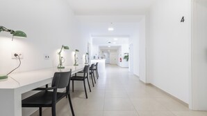Un couloir moderne et bien éclairé, avec une longue table et des chaises, des murs blancs et un design épuré et minimaliste.