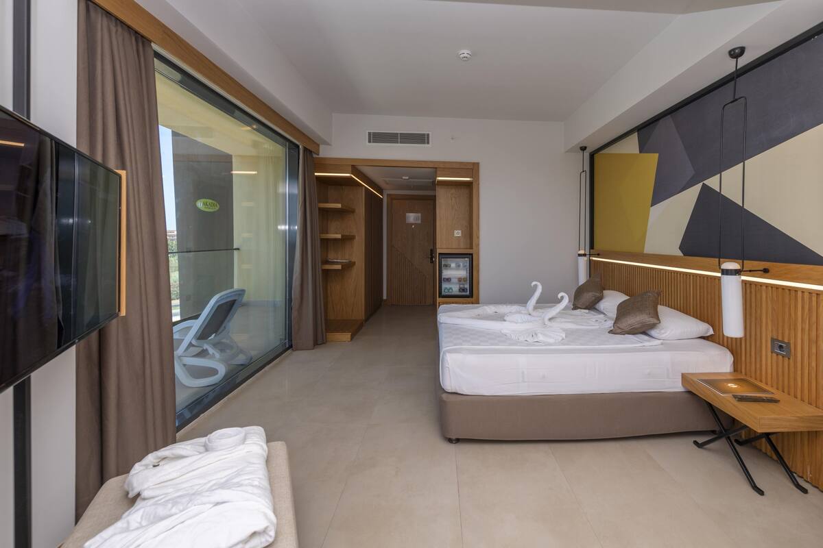 A hotel room with a bed, a TV, a desk, and a large window.