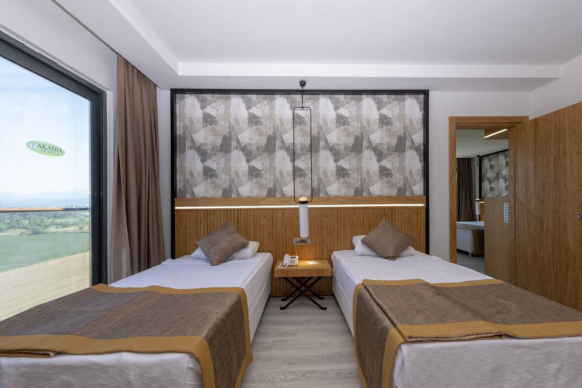 A hotel room with two beds, a small table with a phone, a wall-mounted light, and a view of the outdoors.