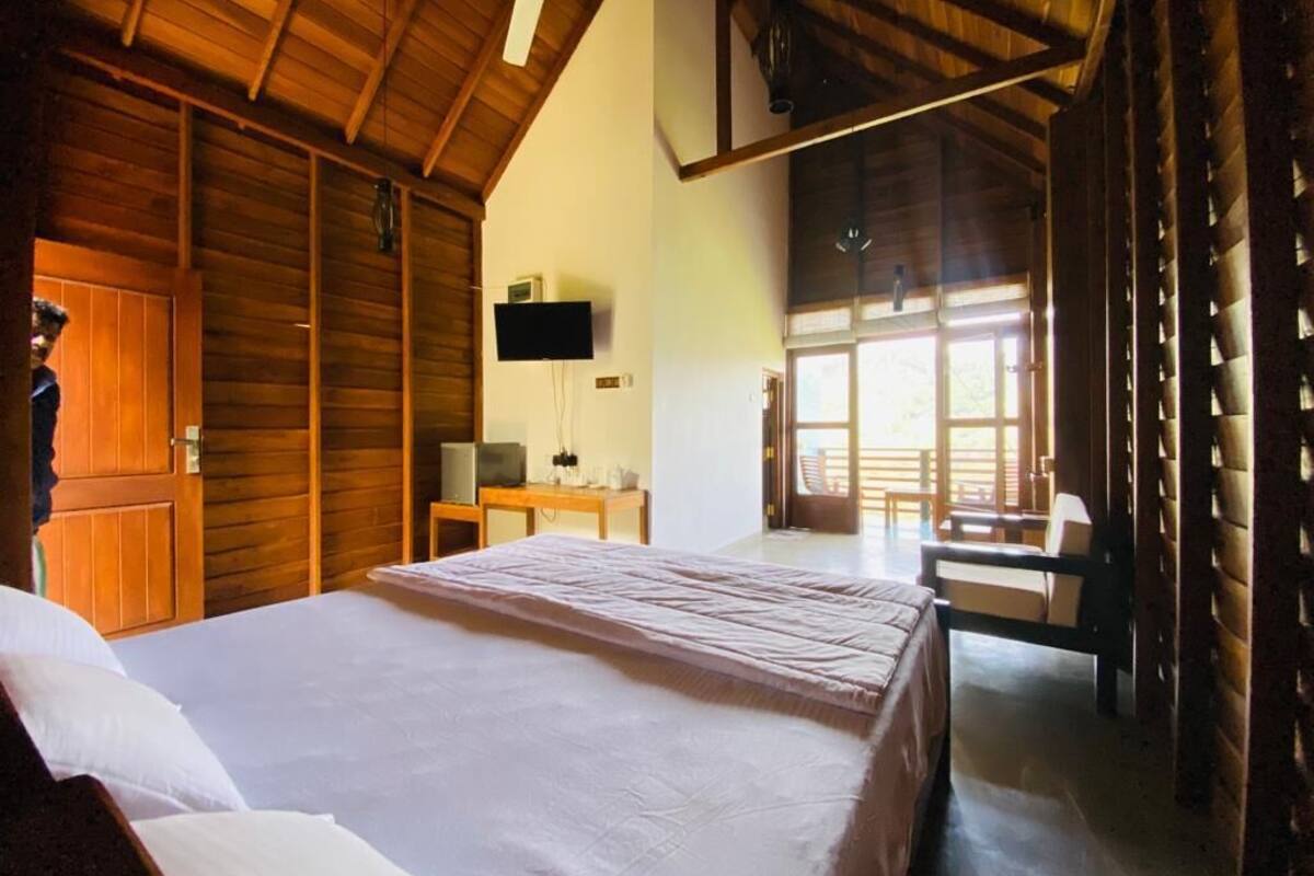 A bedroom with a large bed, wooden walls, a ceiling fan, a TV, and a view of the outdoors.