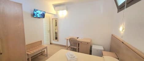A hotel room with a bed, a desk, a chair, a TV, and a mirror.