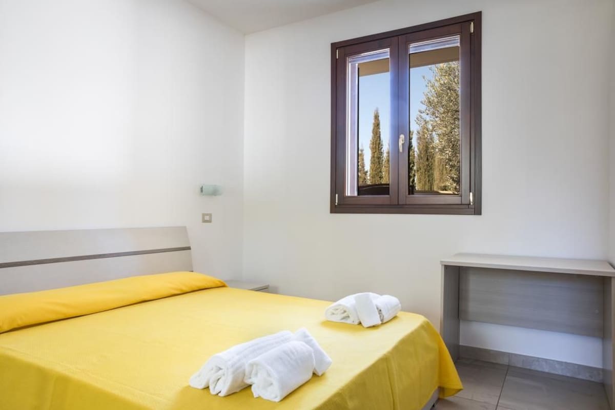 A hotel room with a bed, a nightstand, and a window with a view of trees.