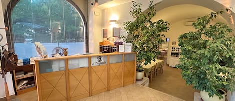 Un espace d’accueil avec un comptoir en bois, une grande fenêtre et des plantes en pot.